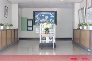 玄関上がりに赤い絨毯が敷かれ、来客用のスリッパが右側に2足並んでおり、中央には机の上に白い花が飾られている来客用玄関の写真