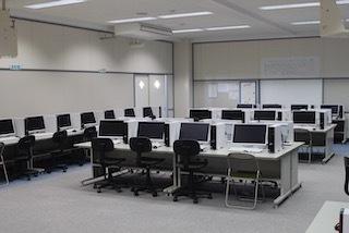 教室の壁側と中央の机の上にパソコンが設置されているコンピューター室の写真